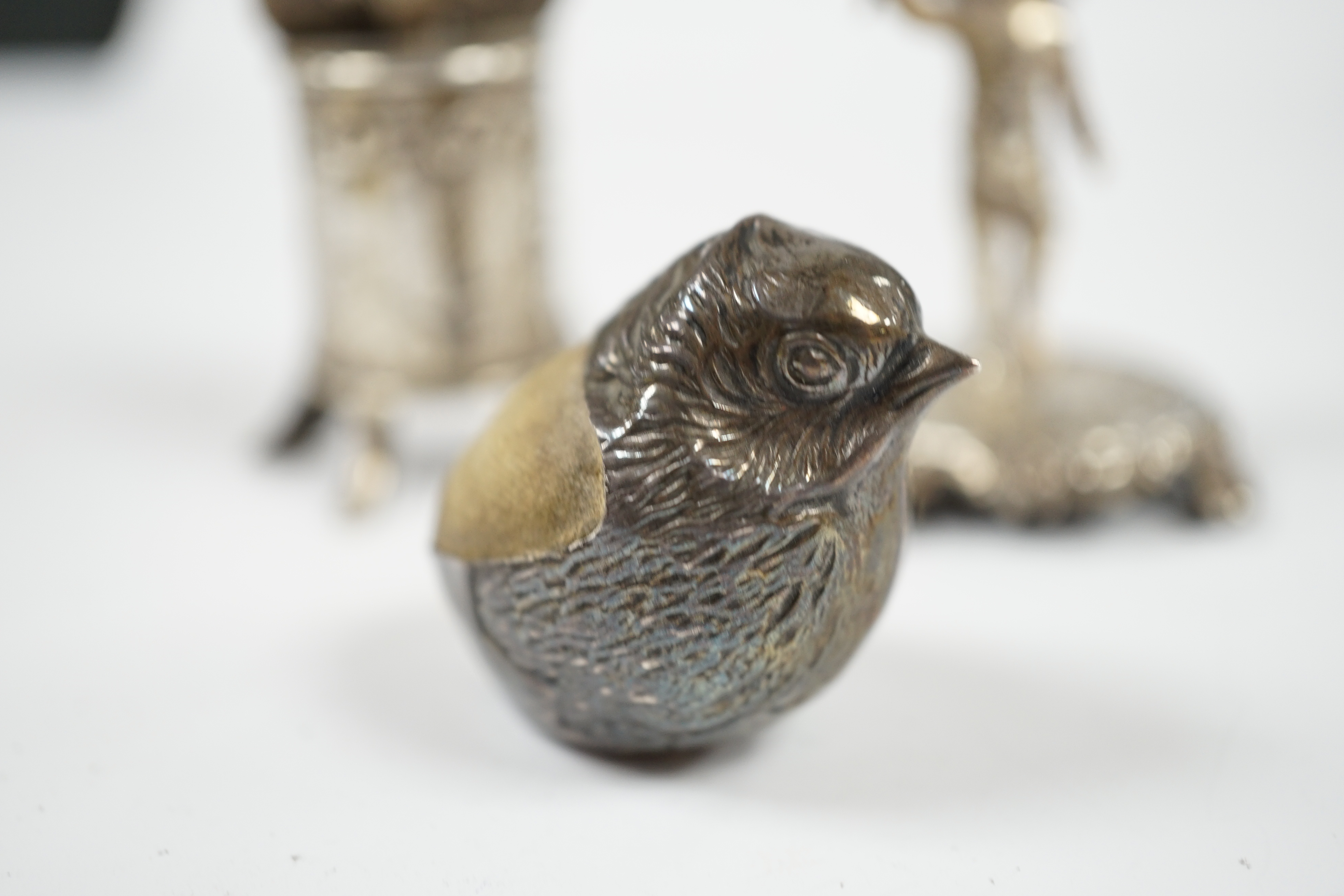 An Edwardian silver mounted 'hatching chick' pin cushion, by Sampson Mordan & Co, Chester, 1908, 29mm, together with two miniature silver groups with import marks. Condition - fair